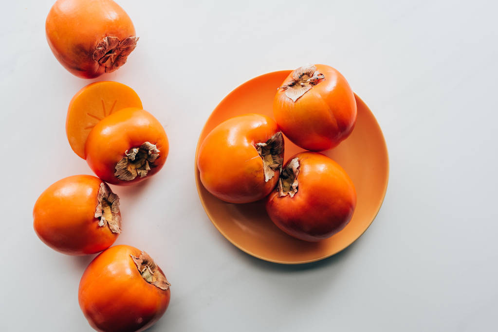 top view of persimmons on orange plate and on white tabletop - Photo, Image