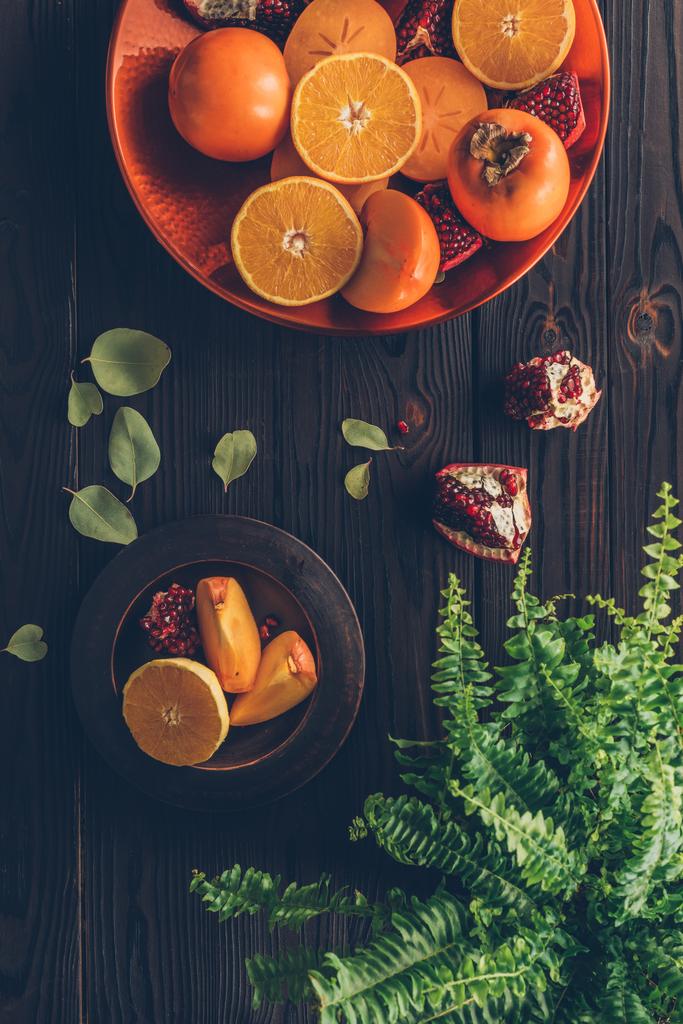 bovenaanzicht van kaki met gesneden sinaasappelen en granaatappels op platen - Foto, afbeelding