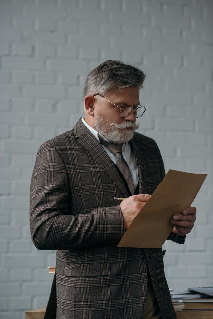 Senior man in tweed pak brief voor witte bakstenen muur - Foto, afbeelding