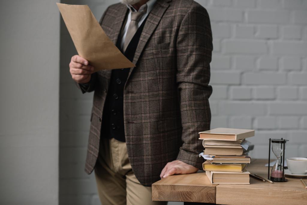 обрезанный снимок человека, читающего письмо во время наклона на рабочем столе
 - Фото, изображение