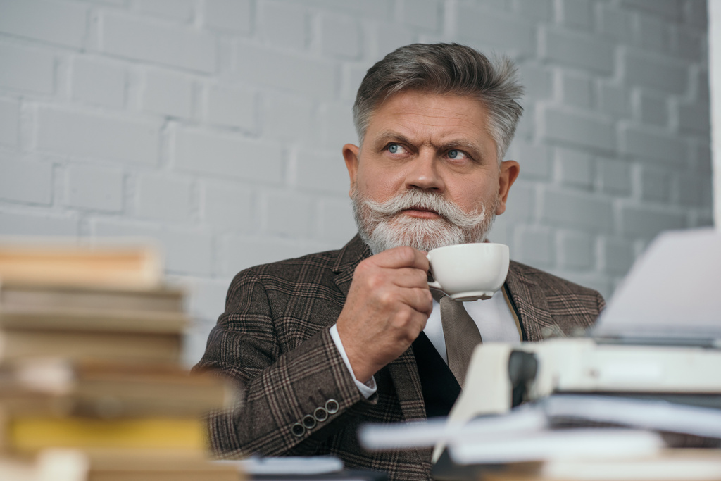 bearded senior writer drinking coffee at workplace - Photo, Image