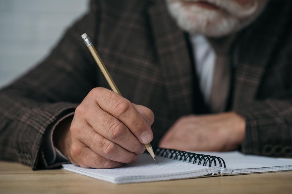 close-up shot of senior man writing in notebook with pencil - Photo, Image