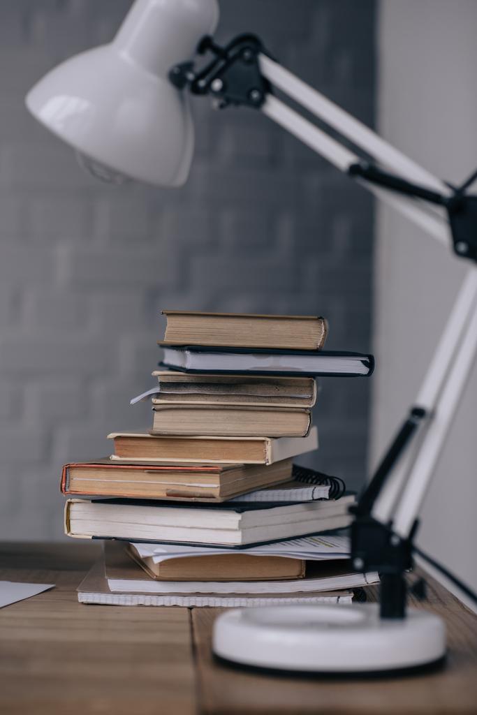 close-up shot of stacked books and table lamp on work desk - Photo, Image