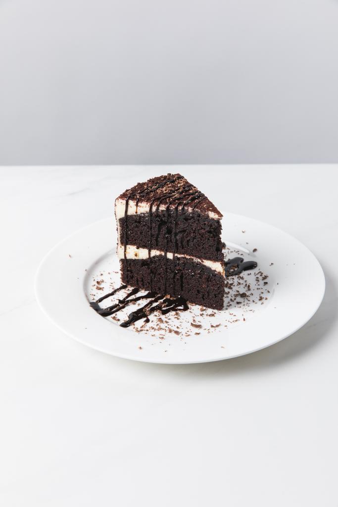 Vista frontal do bolo de chocolate com esmalte na placa colocada na superfície branca
 - Foto, Imagem
