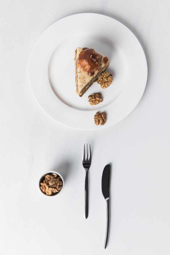 Cake with bowl of walnuts placed on white surface - Photo, Image