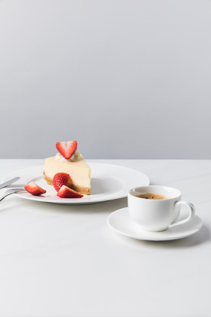 Koffiekopje en bestek in de buurt van plaat met aardbei kwarktaart - Foto, afbeelding