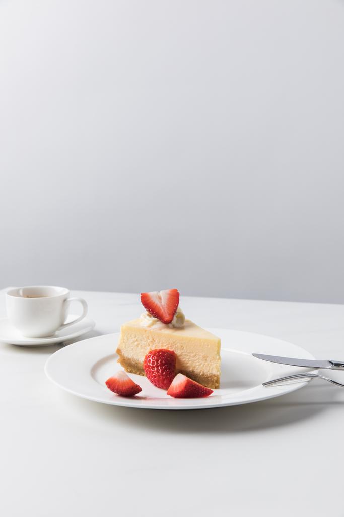Cheesecake with strawberries on plate and cup of coffee on white table - Photo, Image