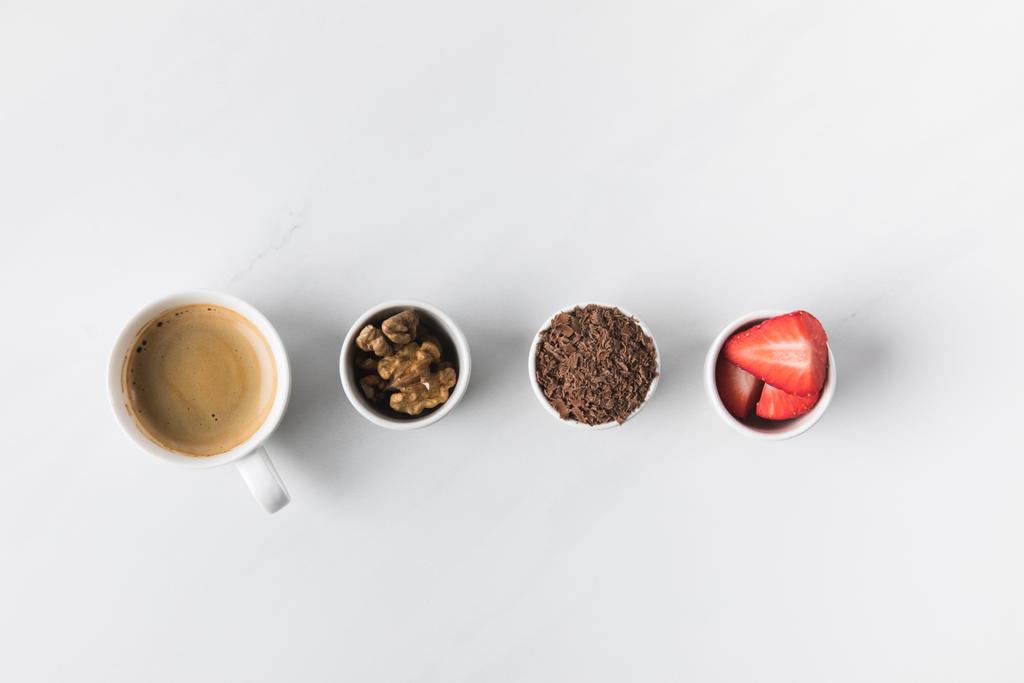 Вид зверху на чашку кави і миски з волоськими горіхами, полуницею і тертим шоколадом
 - Фото, зображення