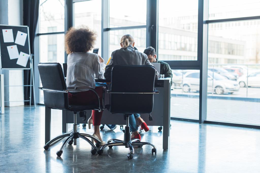 visão traseira de empresários multiculturais sentados à mesa no espaço de trabalho
 - Foto, Imagem