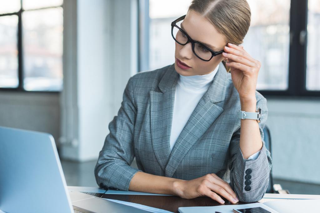 mulher de negócios em óculos olhando para laptop no escritório
 - Foto, Imagem