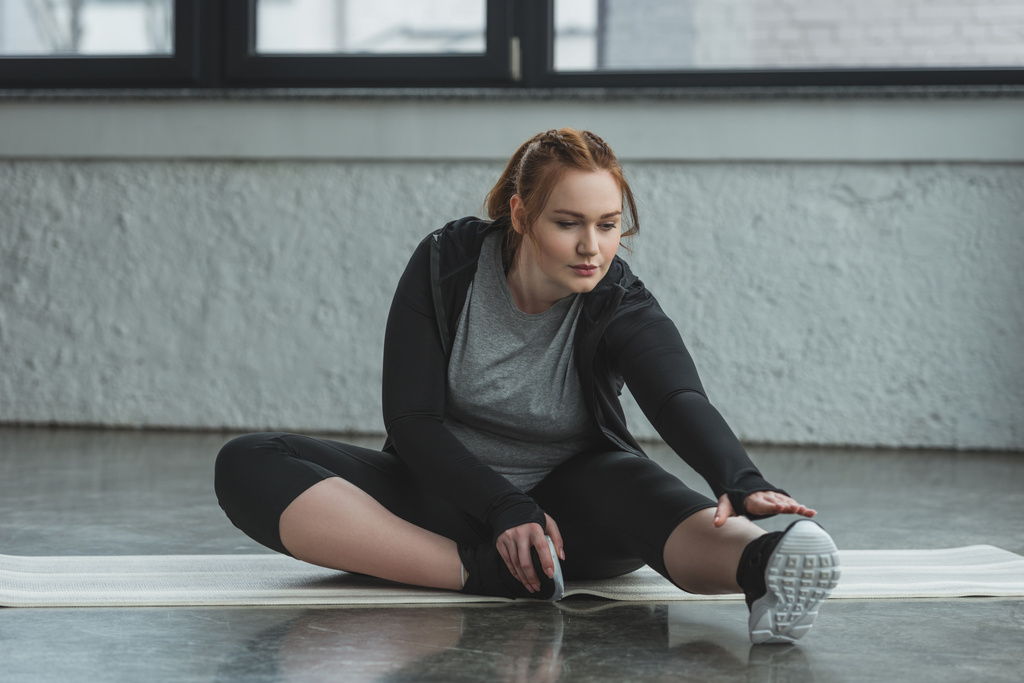 Obese girl stretching on floor in gym - Photo, Image