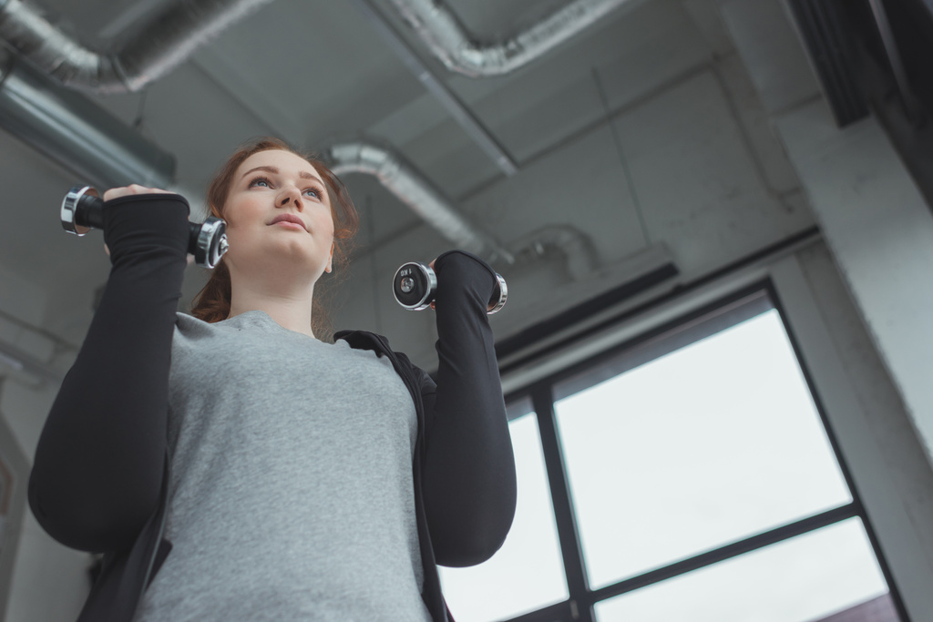 Толстая девушка тренируется с гантелями в спортзале
 - Фото, изображение