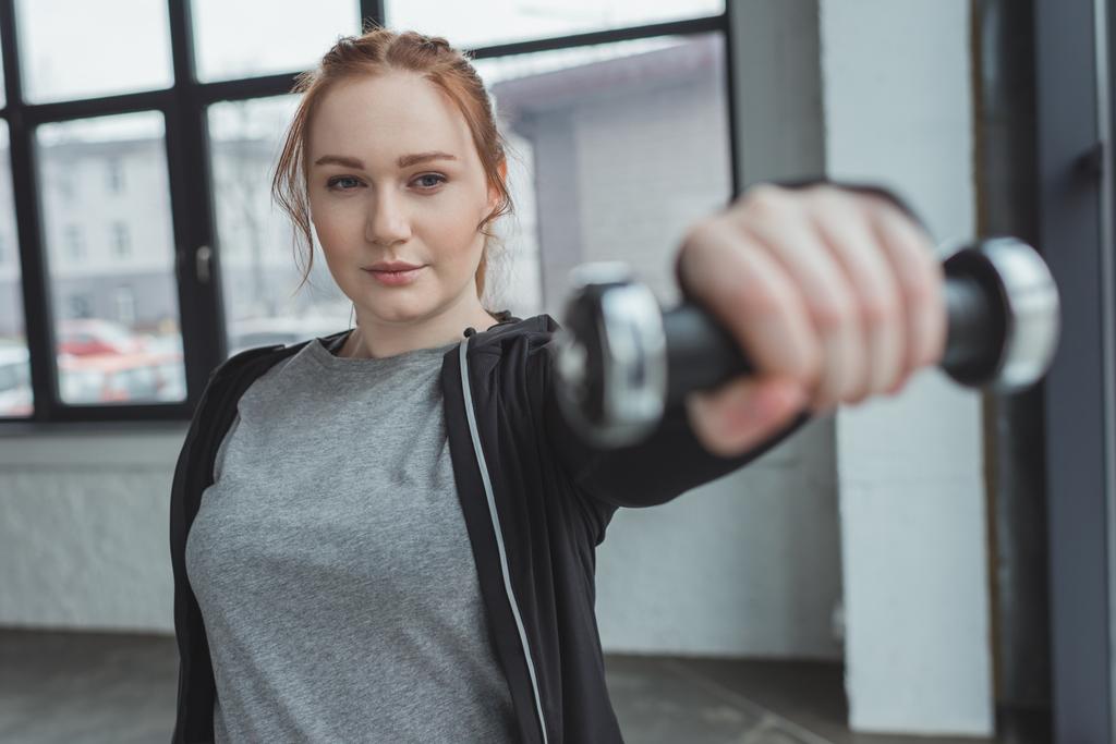 Chica con sobrepeso levantando mancuerna en el gimnasio
 - Foto, imagen