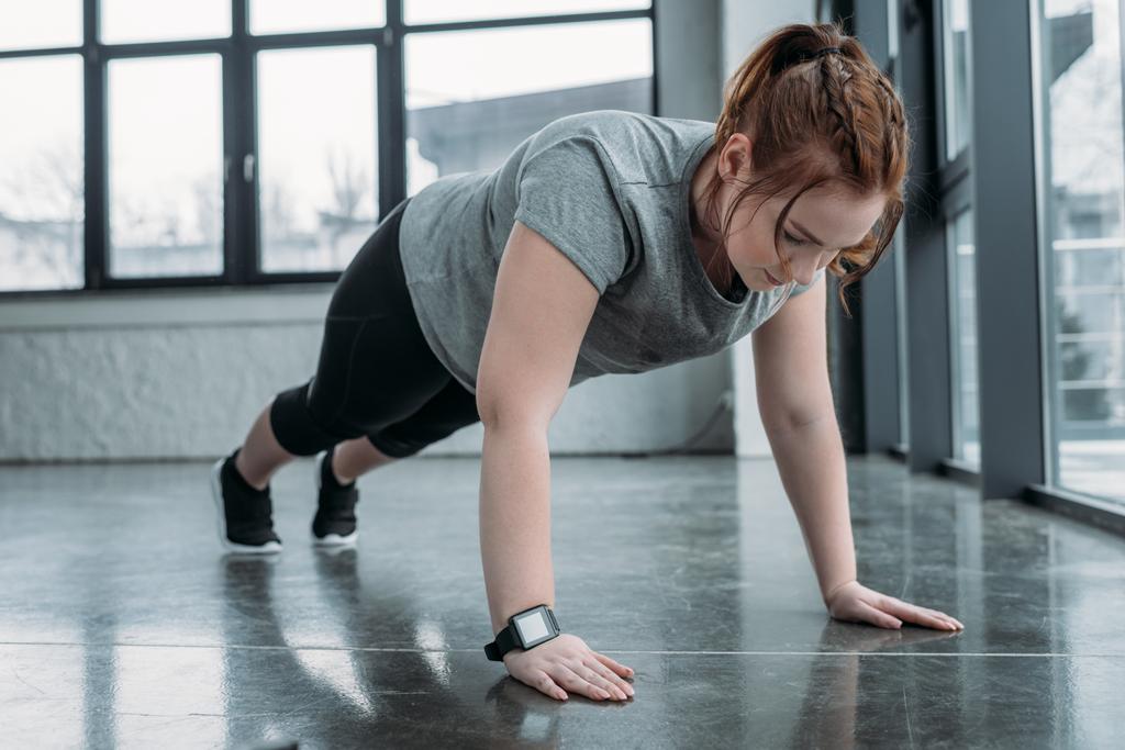Chica con sobrepeso realizando flexiones en el gimnasio
 - Foto, Imagen