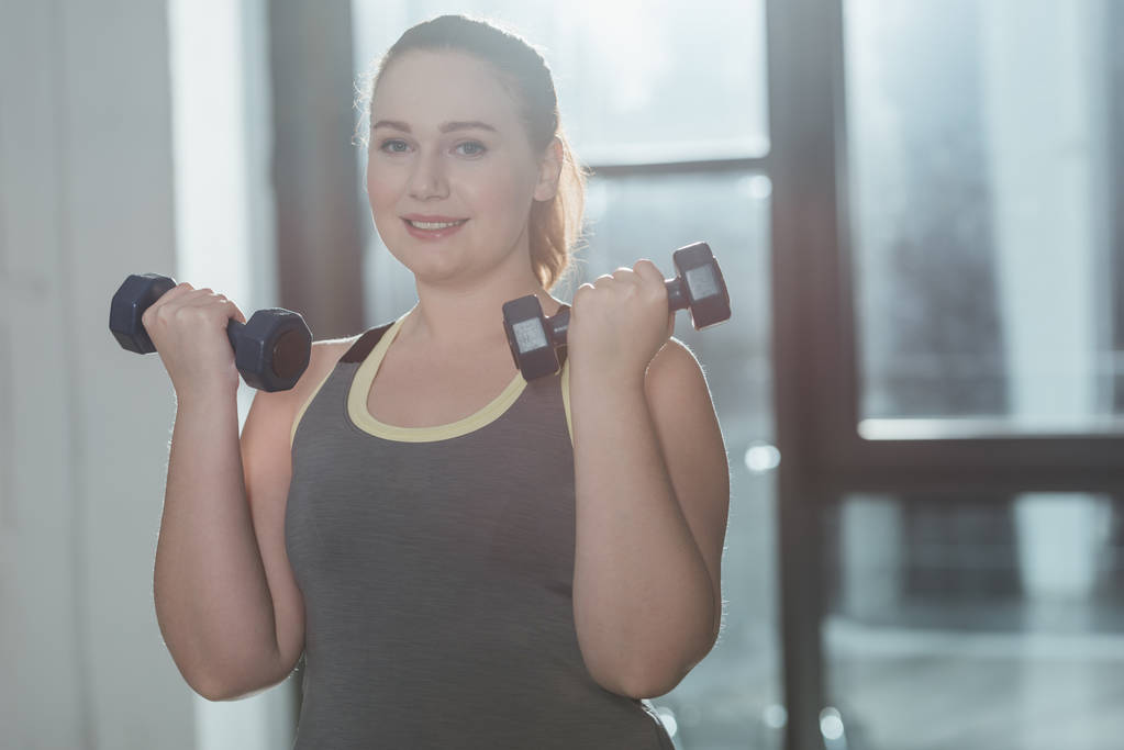 übergewichtige Mädchen beim Training mit Kurzhanteln im Fitnessstudio - Foto, Bild