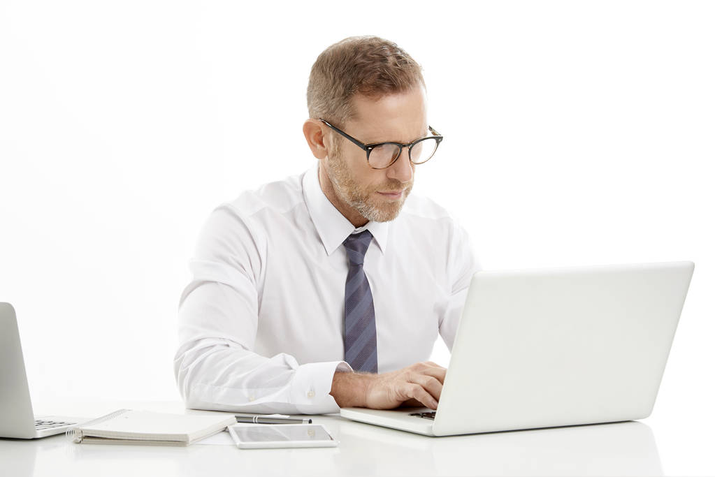 Studiový portrét investiční podnikatel pracuje na notebooku při sezení u stolu v izolované bílé pozadí - Fotografie, Obrázek