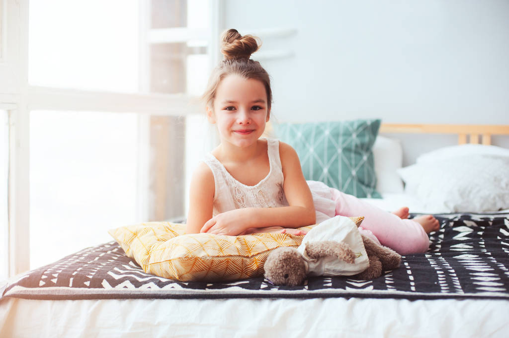 幸せな子女の子目を覚ます朝早く彼女の部屋で居心地の良い家庭的なインテリアで快適なベッドに横になっています。 - 写真・画像