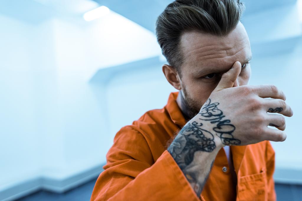 prisioneiro tatuado cobrindo rosto com a mão
 - Foto, Imagem