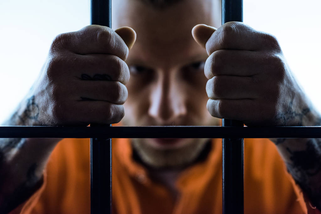 злой заключенный держит тюремные решетки и смотрит в камеру
 - Фото, изображение