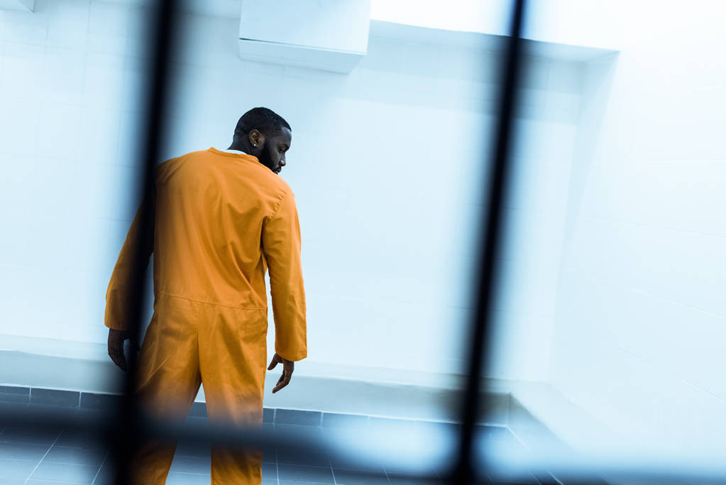 vista trasera del prisionero afroamericano en celda de prisión
 - Foto, imagen