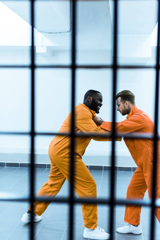 вид збоку мультикультурних в'язнів, що загрожують один одному за ґратами в'язниць
 - Фото, зображення
