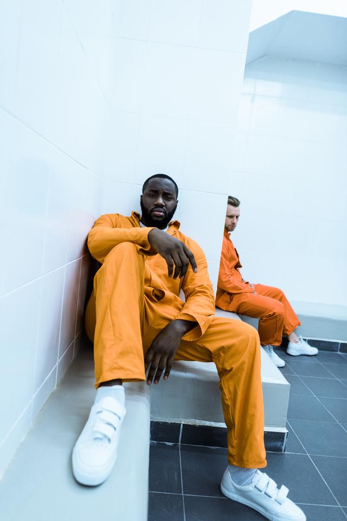 мультикультурные заключенные сидят на скамейках в тюремной камере
 - Фото, изображение