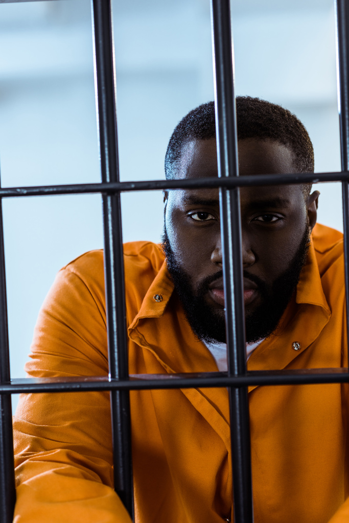Afryki amerykański więzień patrząc na aparat za kratami więzienia - Zdjęcie, obraz