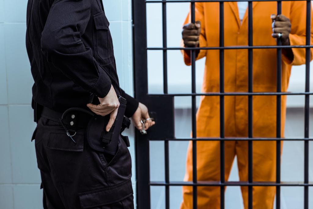 περικομμένη εικόνα δεσμοφύλακα βάζοντας χέρι όπλο κοντά φυλακής τα σίδερα - Φωτογραφία, εικόνα