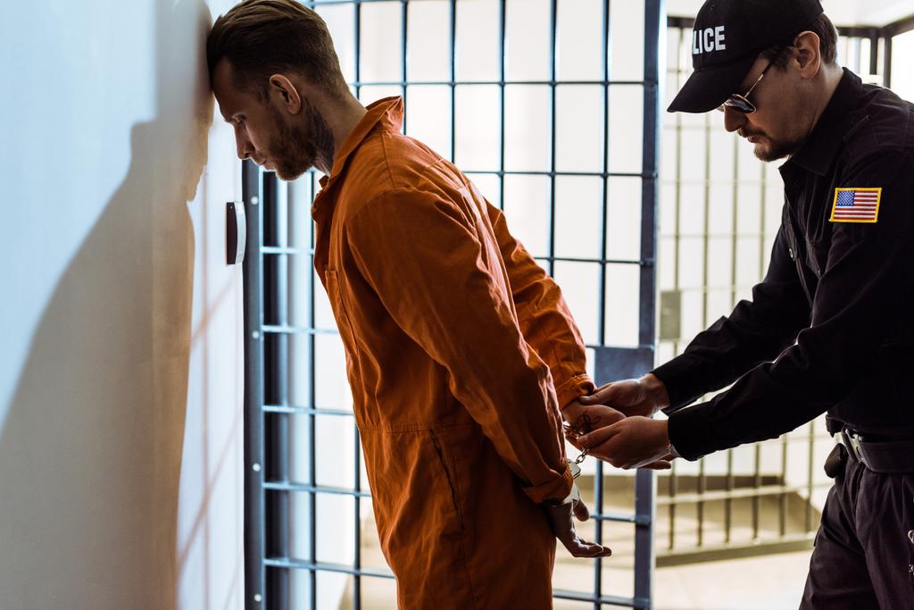 Μερική άποψη του αξιωματικός φυλακής φορώντας χειροπέδες στον κρατούμενο στο διάδρομο - Φωτογραφία, εικόνα