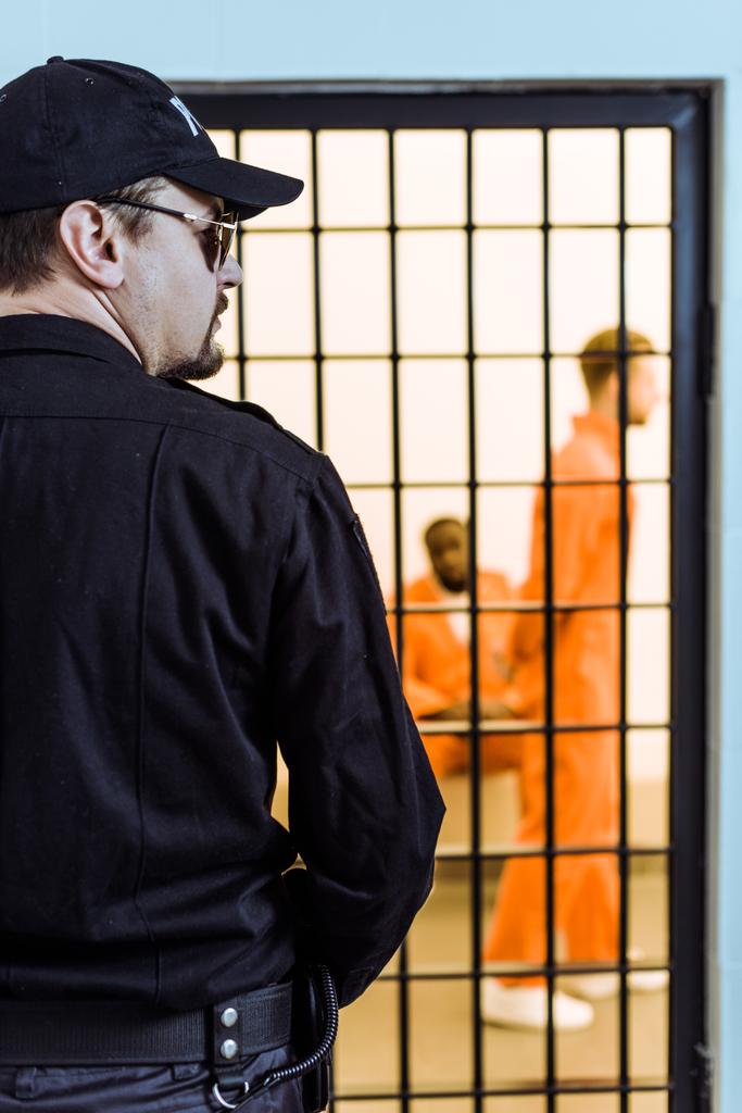 vue arrière d'un agent de la prison se tenant près d'une cellule avec des détenus multiculturels
 - Photo, image