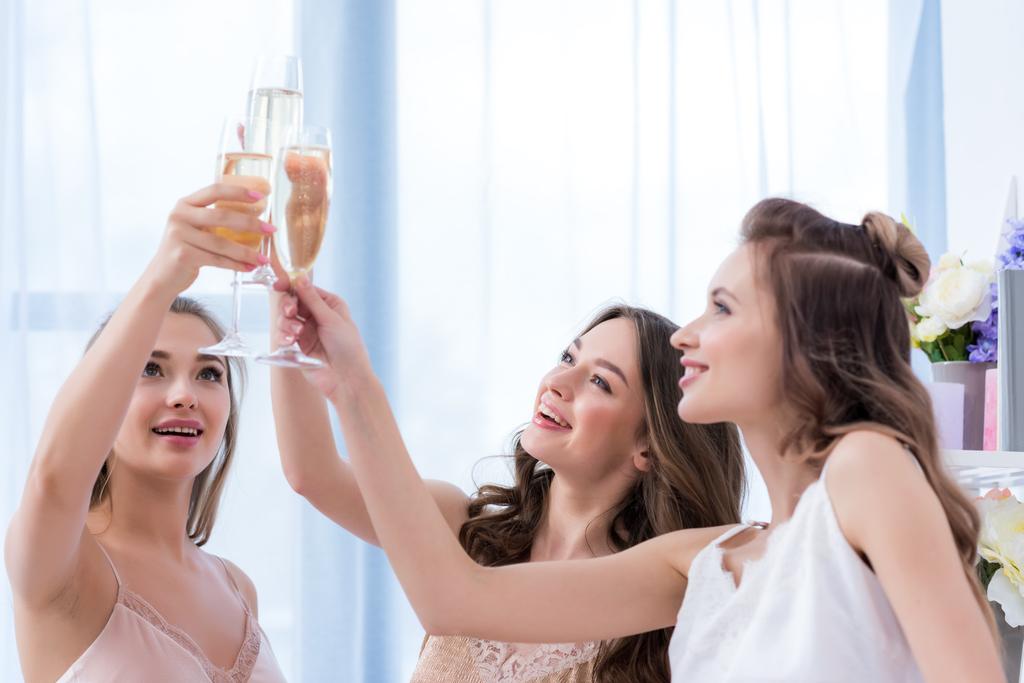 krásné mladé ženy v pyžamu cinkání sklenic šampaňského doma - Fotografie, Obrázek