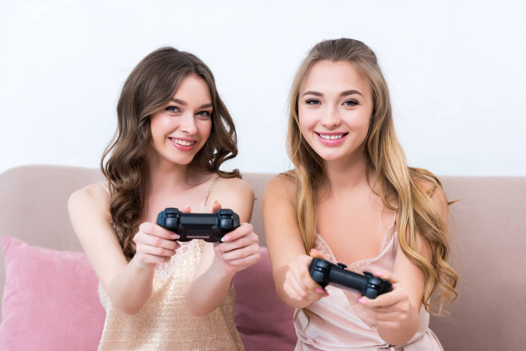 beautiful happy girls in pajamas playing with joysticks and smiling at camera - Photo, Image