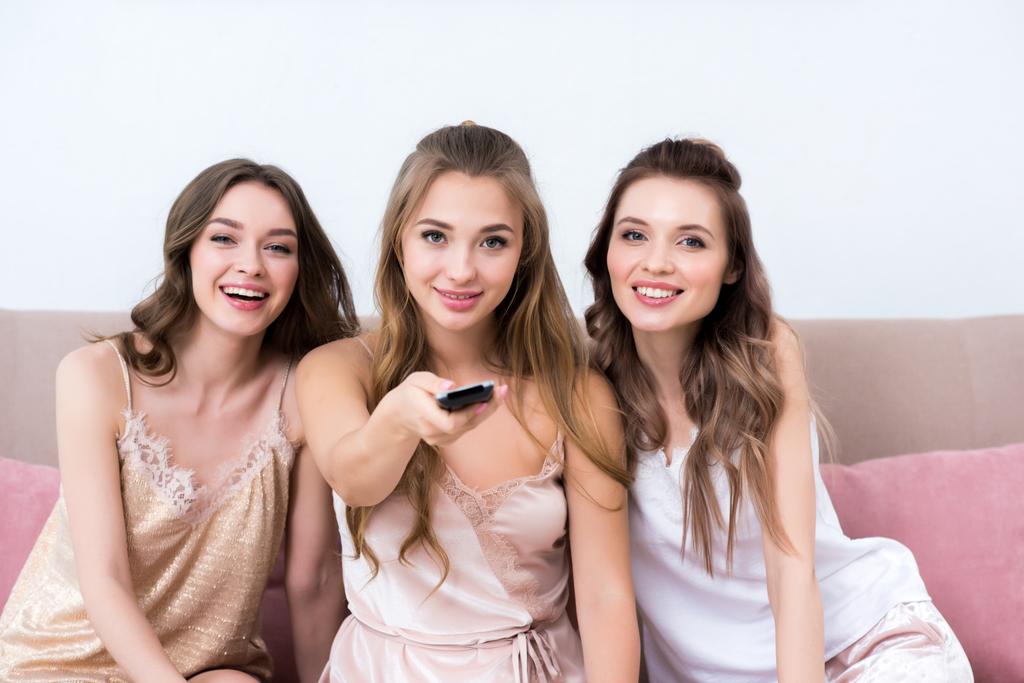 hermosas mujeres jóvenes en pijama usando mando a distancia y sonriendo a la cámara
 - Foto, Imagen