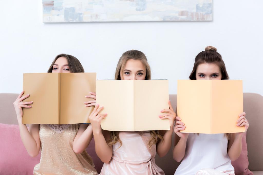drei attraktive Freundinnen halten Zeitschriften in der Hand und blicken in die Kamera - Foto, Bild