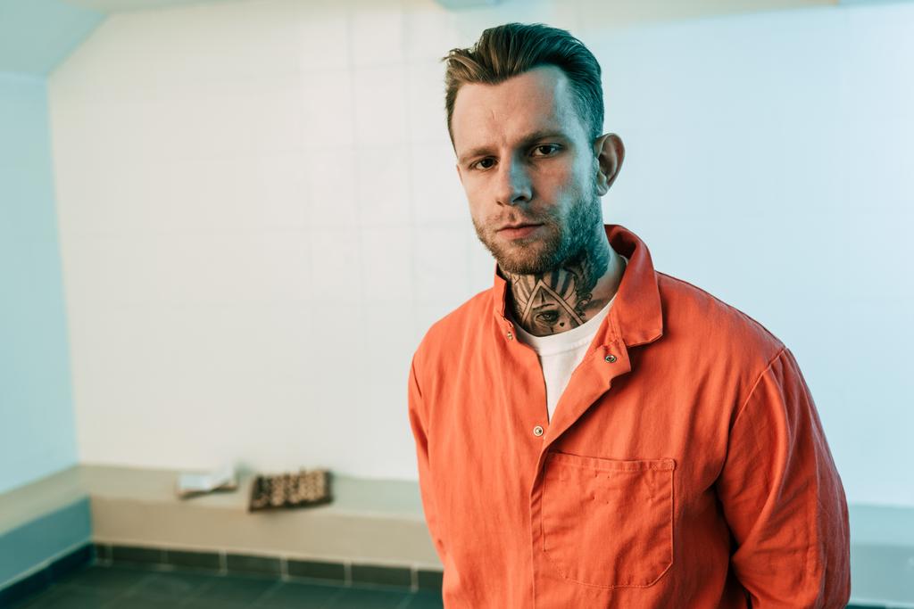 Tetovaný vězeň při pohledu na fotoaparát ve vězeňské cele - Fotografie, Obrázek