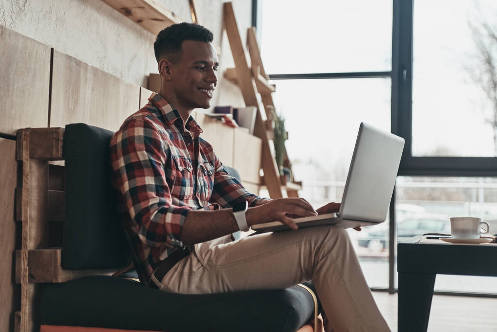 happy African young man using laptop while sitting in creative working space - Photo, Image