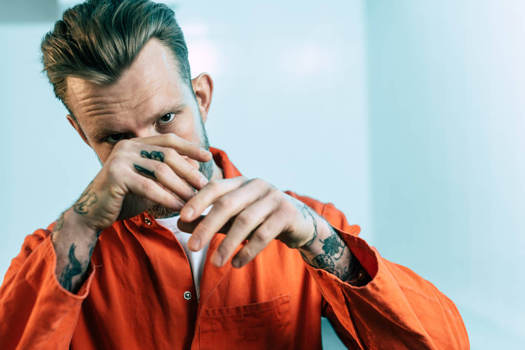 vězeň s tetování pokrývající obličej rukama a při pohledu na fotoaparát - Fotografie, Obrázek