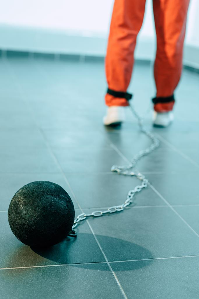 bijgesneden afbeelding van gevangene in oranje uniform met gewicht vastgebonden aan been - Foto, afbeelding