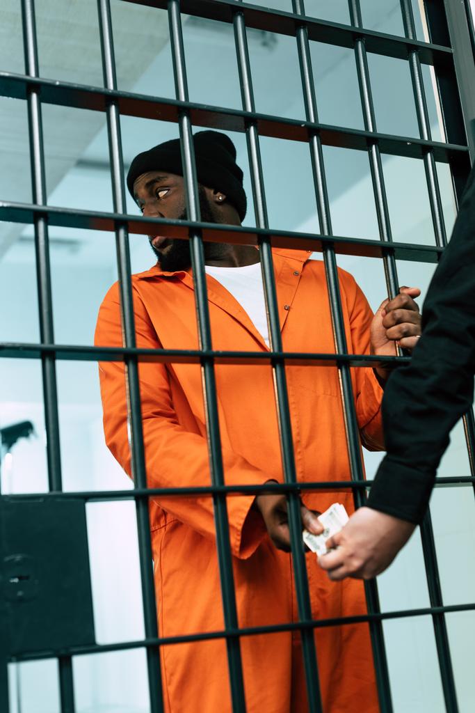 przycięty obraz Afryki amerykański więzień dając pieniądze na straży bezpieczeństwa jako łapówkę - Zdjęcie, obraz