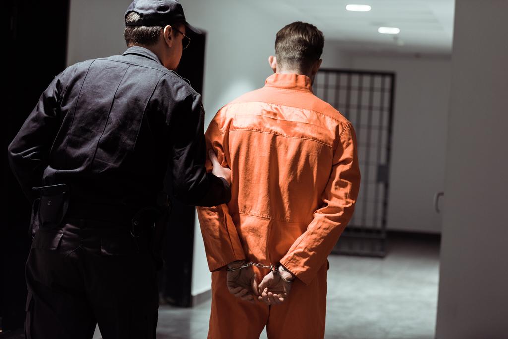 вид ззаду в'язничного офіцера, провідного в'язня в наручниках в коридорі
 - Фото, зображення