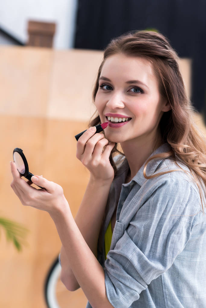 красивая молодая женщина наносит макияж и улыбается в камеру
  - Фото, изображение