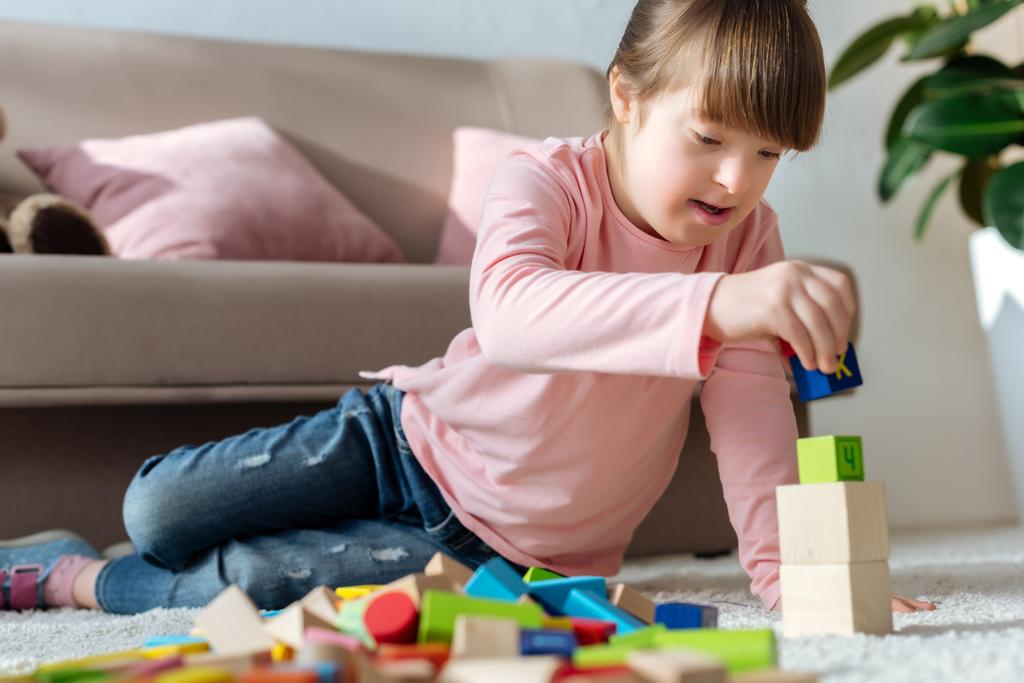 Niño con síndrome de Down jugando con cubos de juguete en el suelo en una habitación acogedora
 - Foto, Imagen