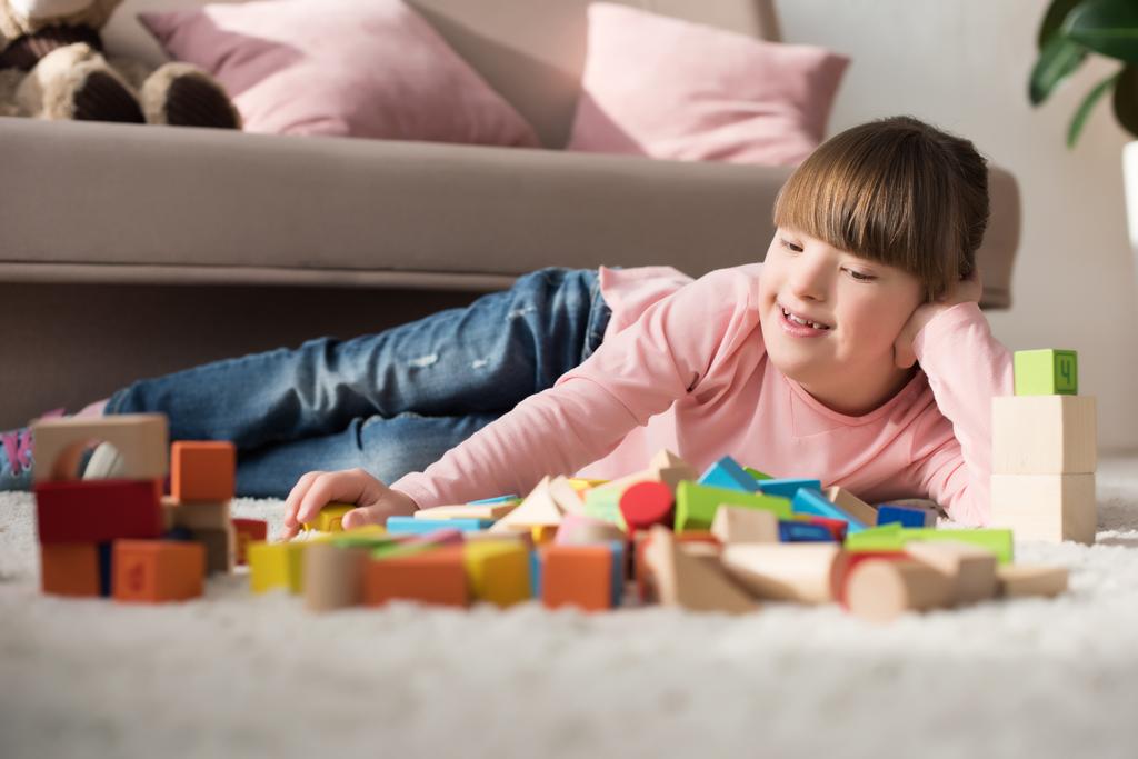 Dziecko z zespołem Downa, leżąc na podłodze i patrząc zabawka kostki - Zdjęcie, obraz