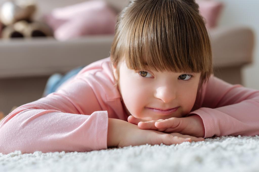 Bambino sognante con sindrome di Down sdraiato sul pavimento in camera accogliente
 - Foto, immagini