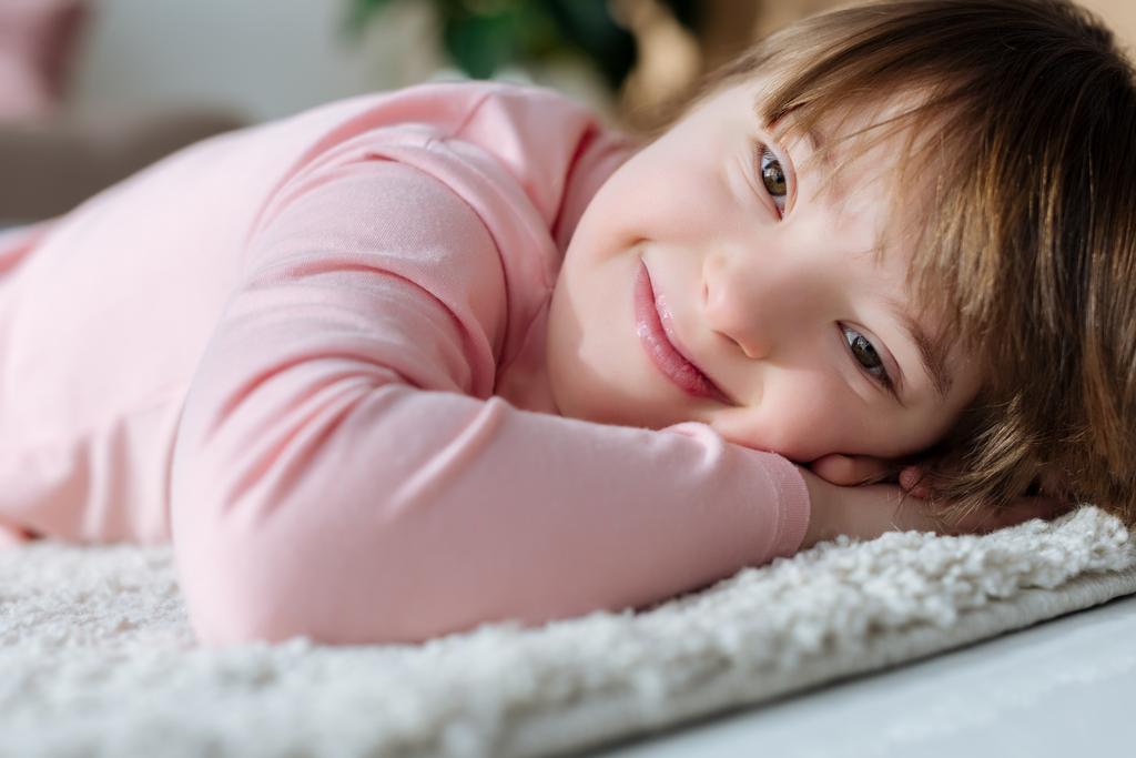 Uśmiechnięte dziewczyny dziecko z zespołem Downa, leżącego na podłodze miękkim dywanie - Zdjęcie, obraz