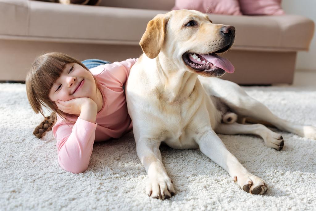 Happy child with down syndrome lying on the floor with Labrador retriever  - Photo, Image