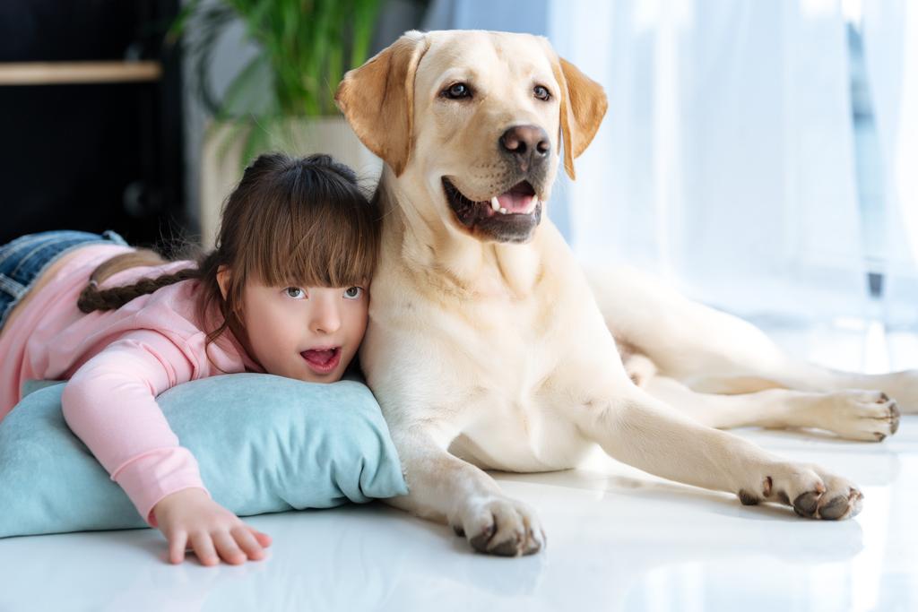 Criança com síndrome de down deitado no chão ao lado do cão Labrador retriever
 - Foto, Imagem