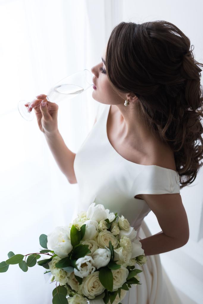 όμορφη νεαρή νύφη με γαμήλια ανθοδέσμη πίνοντας σαμπάνια - Φωτογραφία, εικόνα