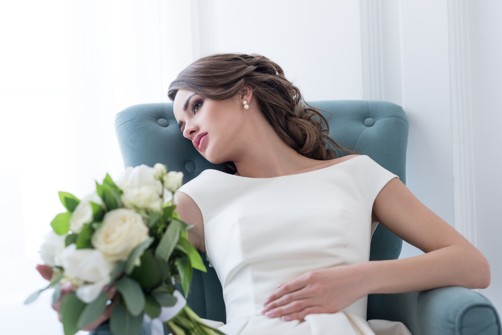 mladá nevěsta s svatební kytice sedí v křesle - Fotografie, Obrázek