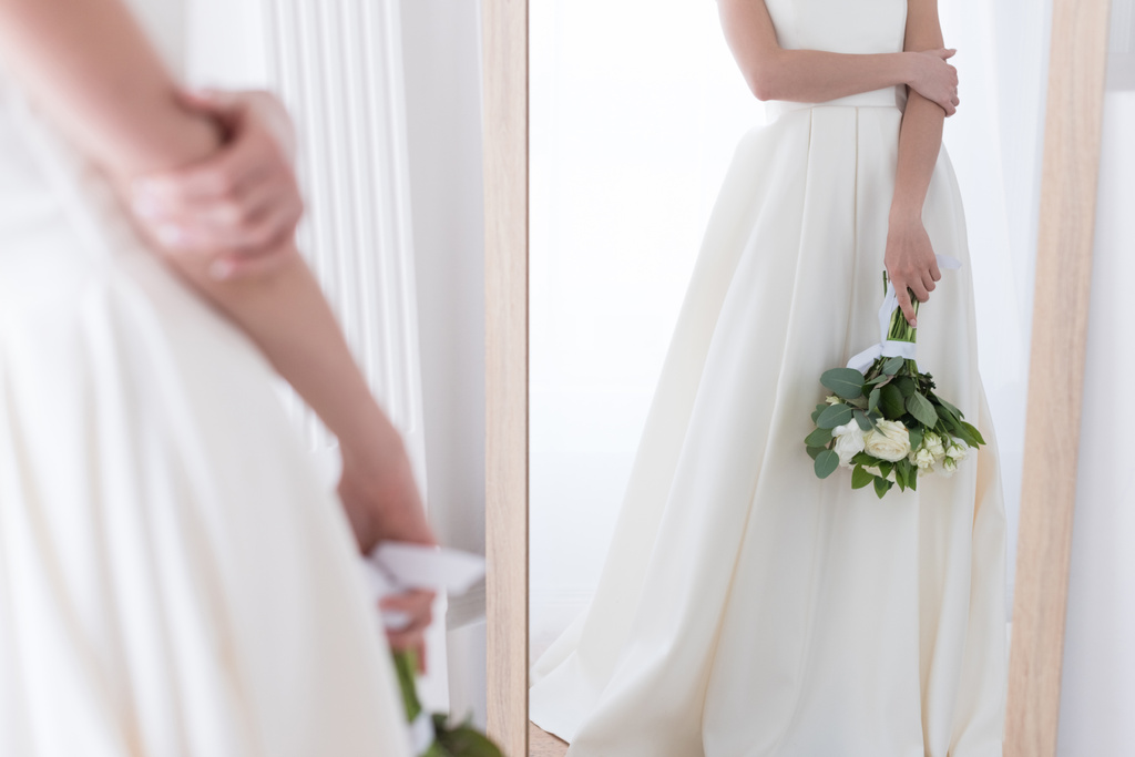 обрізаний вид на наречену в традиційній сукні з весільним букетом, дивлячись на її відображення у дзеркалі
 - Фото, зображення